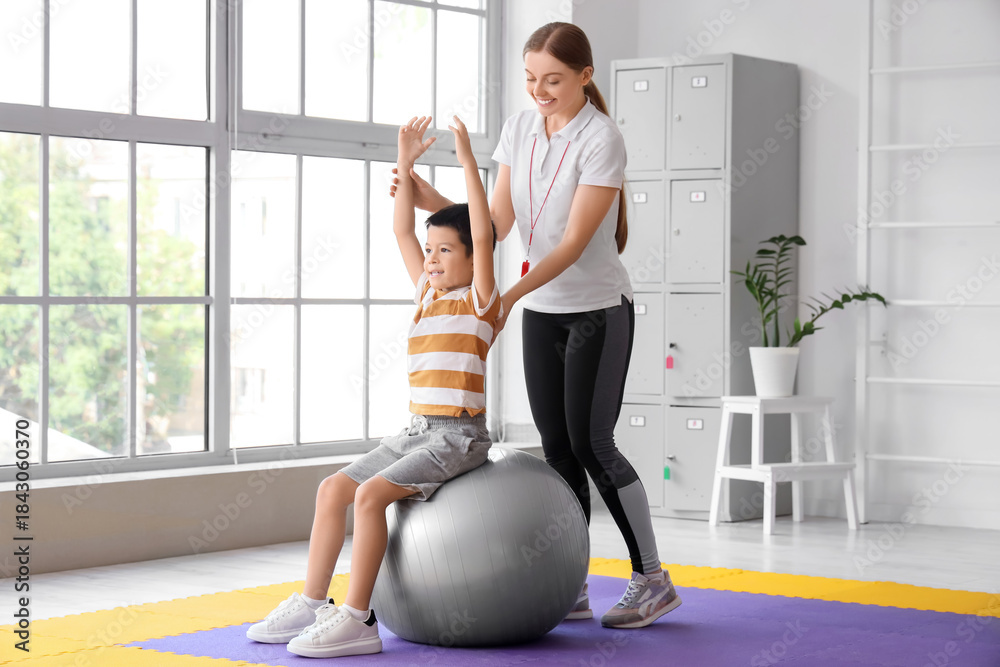 Obraz premium Cute little Asian boy training on fitball with coach in gym