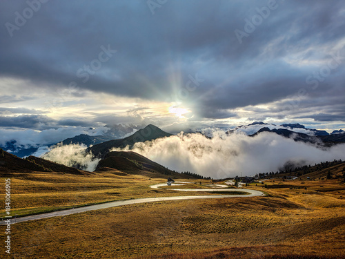 Spectacular sunset over Passo Giau with a mountain winding road crossing golden meadow and foggy valleys. Dolomites, Italy