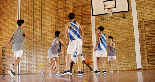 Players closing in school gym after ball landing at gray bib player's feet, contesting possession