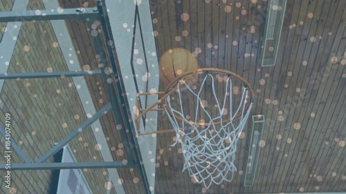 Student shooting for sports, trying to score as ball passing through rim with speckled overlay