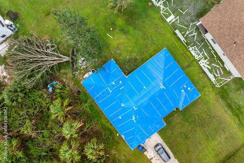 Фотография Aerial view of damaged in hurricane house roof covered with blue protective tarp