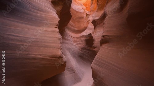 Narrow slot canyon illuminated by sunlight, showcasing its unique sandstone formations and smooth textures in warm natural light.