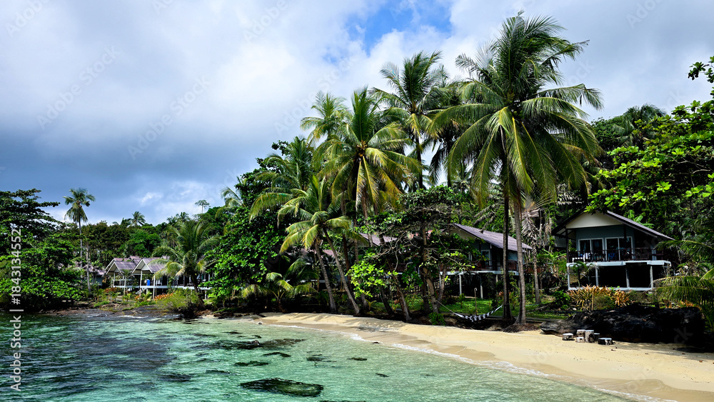 Obraz premium Relax on the serene sands of Koh Kood Island as palm trees sway in the gentle breeze. The crystal-clear water invites visitors to explore this tropical paradise during a sunny day.