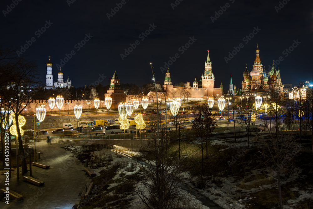 Fototapeta premium Moscow, Russia. View from Zaryadye Park to the Moscow Kremlin, Ivan the Great Bell Tower and St. Basil's Cathedral. Beautiful street lighting and garlands on lanterns. Historical center of Moscow.