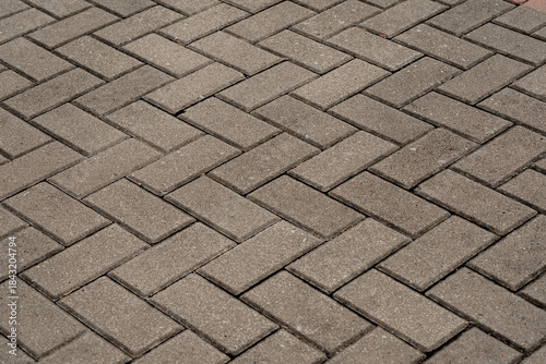 Gray concrete paving blocks arranged in herringbone pattern forming a textured sidewalk surface.