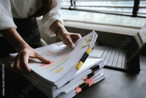 Фотография A woman reviews and organizes a stack of documents with sticky notes at her desk, working carefully in an office with natural light