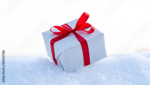 White gift box with red ribbon on snowy surface
