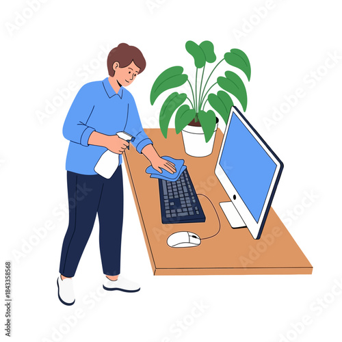 Diligent young man cleaning office desk, keyboard, and monitor with spray bottle and microfiber cloth.