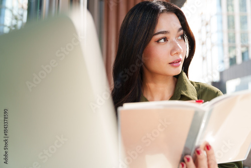 Free Download Young beautiful, elegant Asian woman in brown shirt hold notebook, looking away, thinking with computer laptop in luxury cafe. Digital technology, modern lifestyle, online learning and hybrid working - GFXLoad