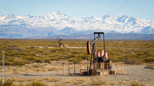 Oil pumpjack operating in an arid field with the Andes mountains in the background, Argentina.
