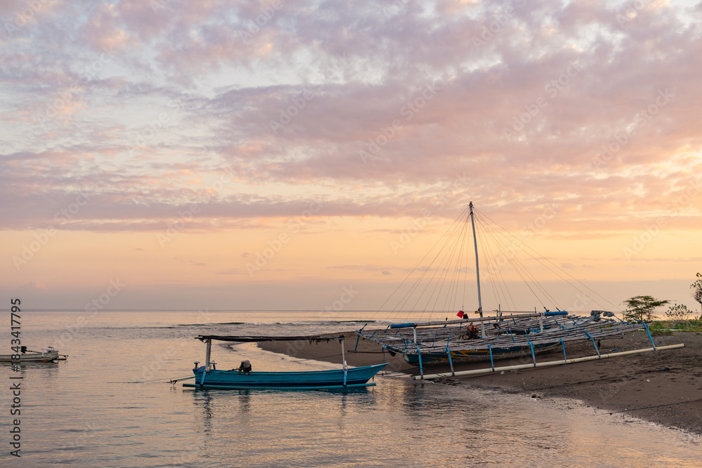Fototapeta premium Tranquil beach scene with outrigger boats resting on the shore under a pastel-colored sky