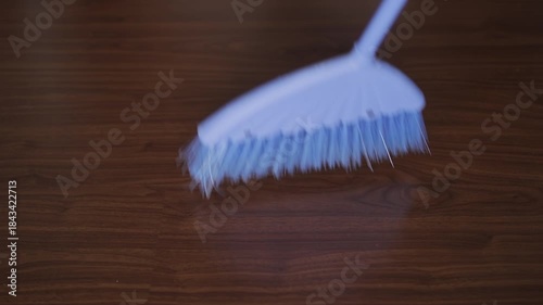 Broom with synthetic bristles sweeping dust and debris from a wooden laminate floor. Housekeeping and domestic chores concept