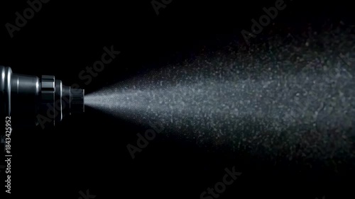 Metal spray nozzle releasing fine mist droplets into dark studio background with side lighting