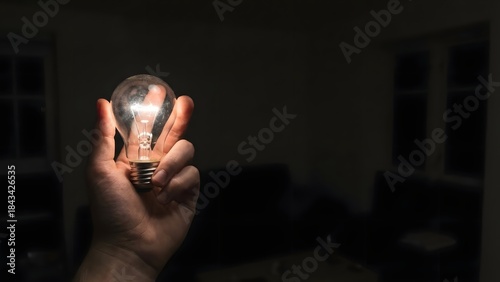 Person Holding Bright Light Bulb in Dark Room.
