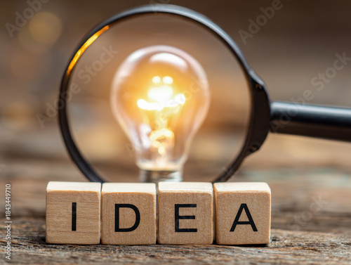 Fototapeta Wooden letter blocks spelling idea with a glowing light bulb magnified by a handheld magnifying glass symbolizing creativity and innovation concepts