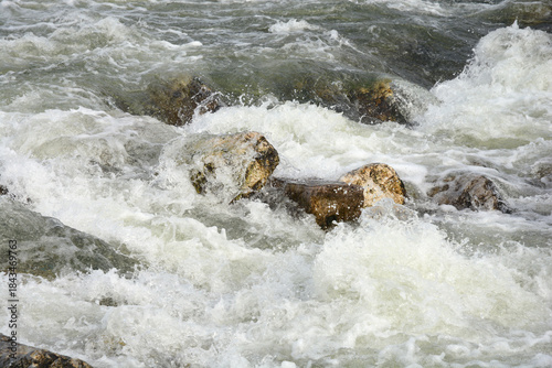 Φωτογραφία Close-up of white, foamy water churning and splashing around large mossy rocks i