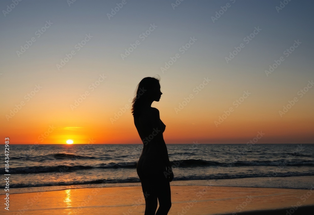 Fototapeta premium Silhouette of a young woman standing on the beach at sunset