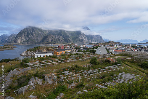 Aerial view of the fishing village of Henningsvaer with fish dryers on a foreground and mountains and water on a background. Norway
