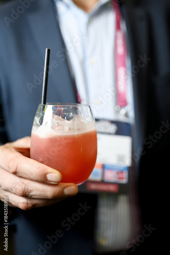 Close-up of a hand holding a stemless glass with a reddish-pink beverage and black straw