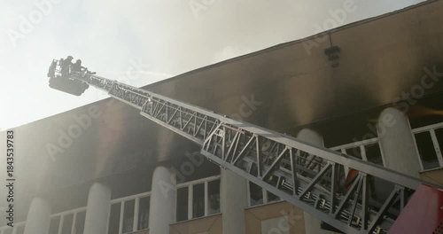 Silhouette of firefighters in a bucket on the ladder of a fire truck, extinguishing with a water gun the roof of a burning building.