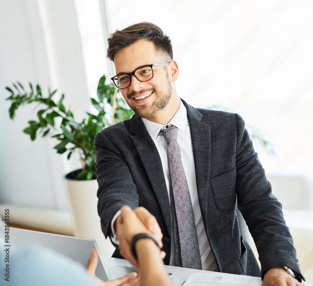 Naklejka premium Happy young businessman shaking hands with a client in the office