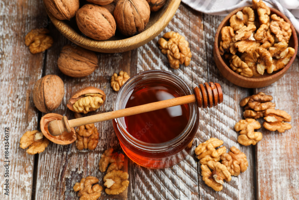 Fototapeta premium Honey in jar, walnuts and dipper on wooden table, above view