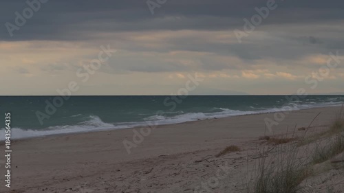 Stormy turquoise sea waves on empty sandy beach at dusk