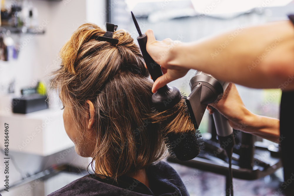 Naklejka premium Woman receiving professional haircut and styling in beauty salon by hairdresser. Hair care ritual, beauty treatment and pampering concept