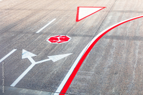 Painted guidance markings on an airport tarmac surface. Directional arrows for vehicles, a mandatory stop sign, and holding lines for aircraft