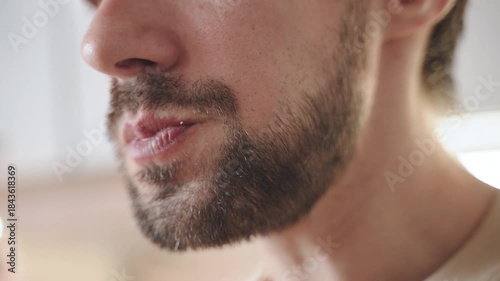 Close up of closed mouth of stubbled man chewing. Slender man chews food and sips tea from mug. Natural process of eating for hispanic male person.