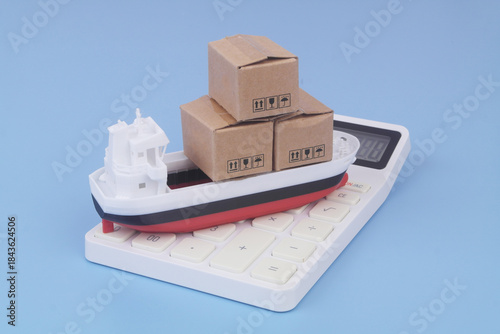 Cargo ship model with boxes on calculator on blue background. Sea ​​transportation budget and price concept.