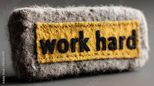 Gray Felt Object with 'Work Hard' Yellow Patch on Neutral Background