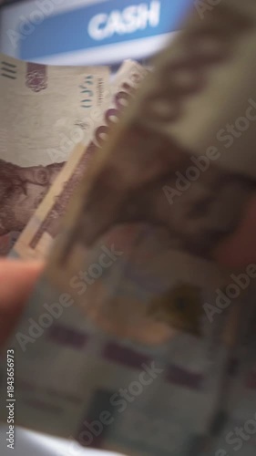 A close-up of a person's hand withdrawing money from an ATM. Ukrainian currency.
