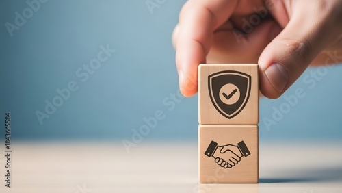 A hand placing a wooden block with a shield and checkmark on top of another block with a handshake