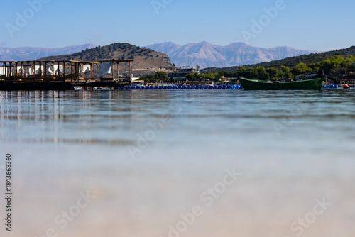 Tranquil sea surface with distant beach facilities, mountains and sky at Ksamil, Albania. Copyspace for text