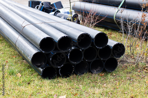 Grasscovered outdoor area featuring stacked black plastic pipes illuminated by early sunlight