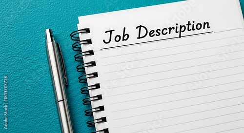 Job description written on lined paper next to a silver pen on teal surface