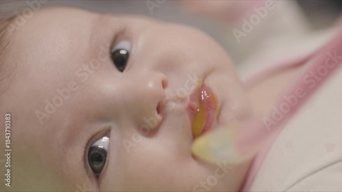 Close-up of newborn baby girl eating medication from a pink spoon