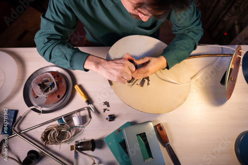 Billede på lærred Craftsman upcycle master disassembling vintage electric lamp at workshop, man preparing item parts for repairing and inspection, taking out light bulb socket off lampshade, refurbishing and reuse