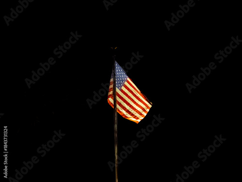 Illuminated American flag flying  on pole at night with black background