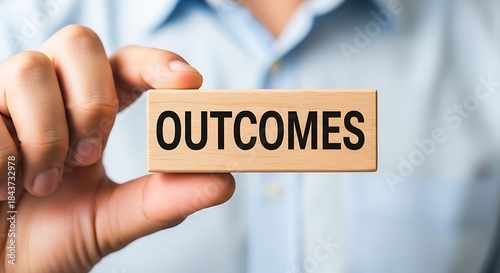 Businessman holding a wooden block with the word outcomes emphasizing results and final goals in business strategy