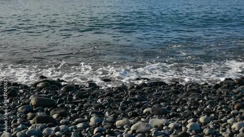 waves of the Atlantic Ocean splashing on a pebble beach in Madeira, Spain