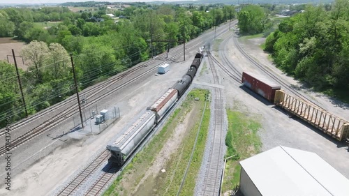 A vintage steam freight train makes its way backing up in yard performing switching operations moving steadily along the railway tracks in a peaceful countryside setting.