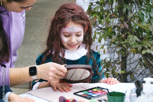 Billede på lærred A little girl and a make-up artist after having applied face paint and decorativ