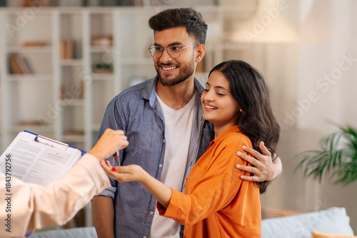 Fotografia Real estate agent giving keys to young indian buyers, happy woman taking key of