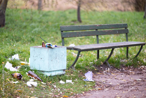 A trash can is positioned right next to a bench that is located in a park. High quality photo