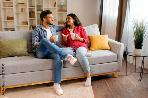 Schilderij op canvas Happy Indian couple drinking coffee and having conversation, enjoying weekend to