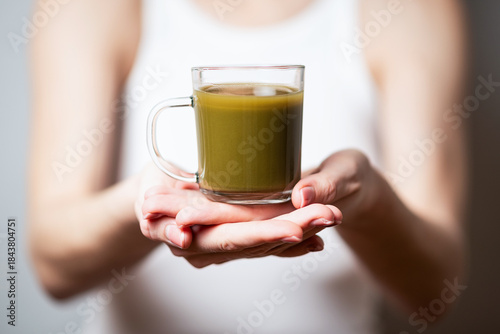 Kratom consumption concept:  female holds a ready to drink glass of green liquid, powdered kratom melted in hot water, kratom tea, close up photo, selective focus