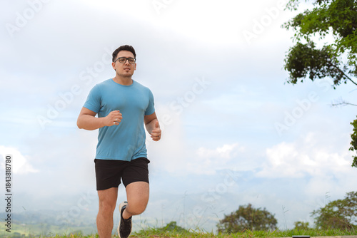 Man jogging outdoors on a hill under cloudy sky as part of cardio fitness training routine