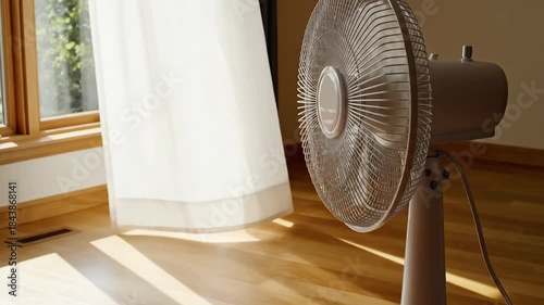 A standing fan circulates air in a sunlit room with flowing white curtains casting shadows on